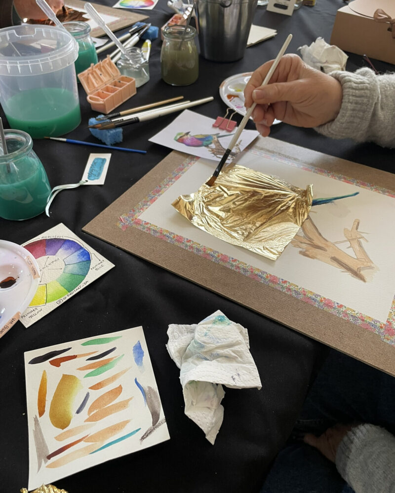 A participant applying gold-coloured detail to artwork at a workshop table.