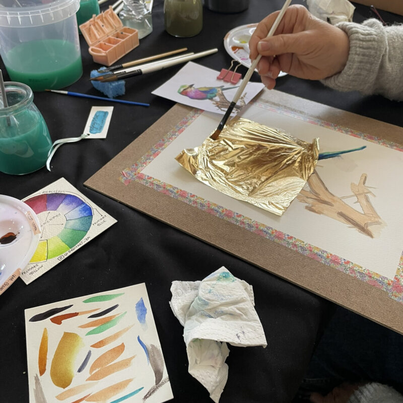 A participant applying gold-coloured detail to artwork at a workshop table.