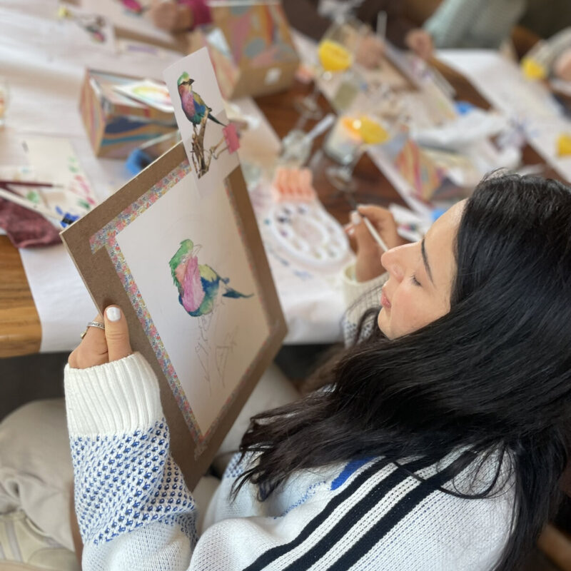 A participant painting a colourful bird while other people work in the background.