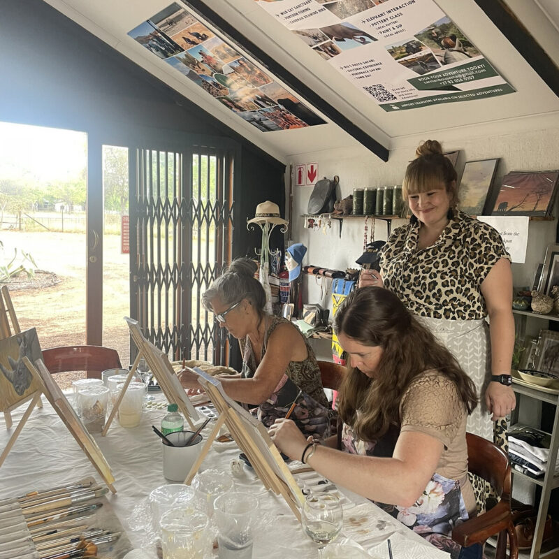 People painting at tables with small easels in a bright workshop room.