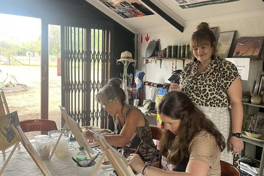 People painting at tables with small easels in a bright workshop room.