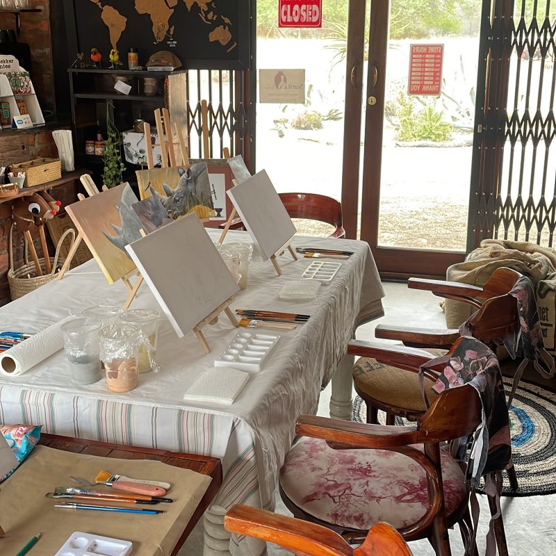 A long table set with easels, canvases and palettes, ready for a workshop.