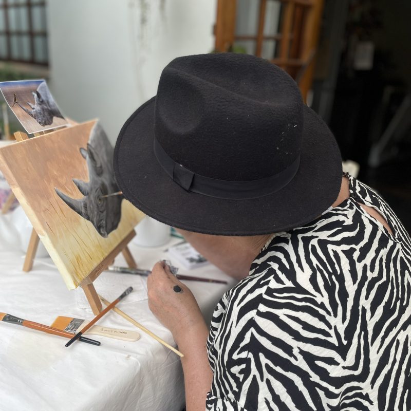 A participant painting an animal on canvas at a tabletop easel.