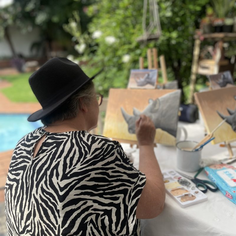 A participant painting at a tabletop easel beside a swimming pool.