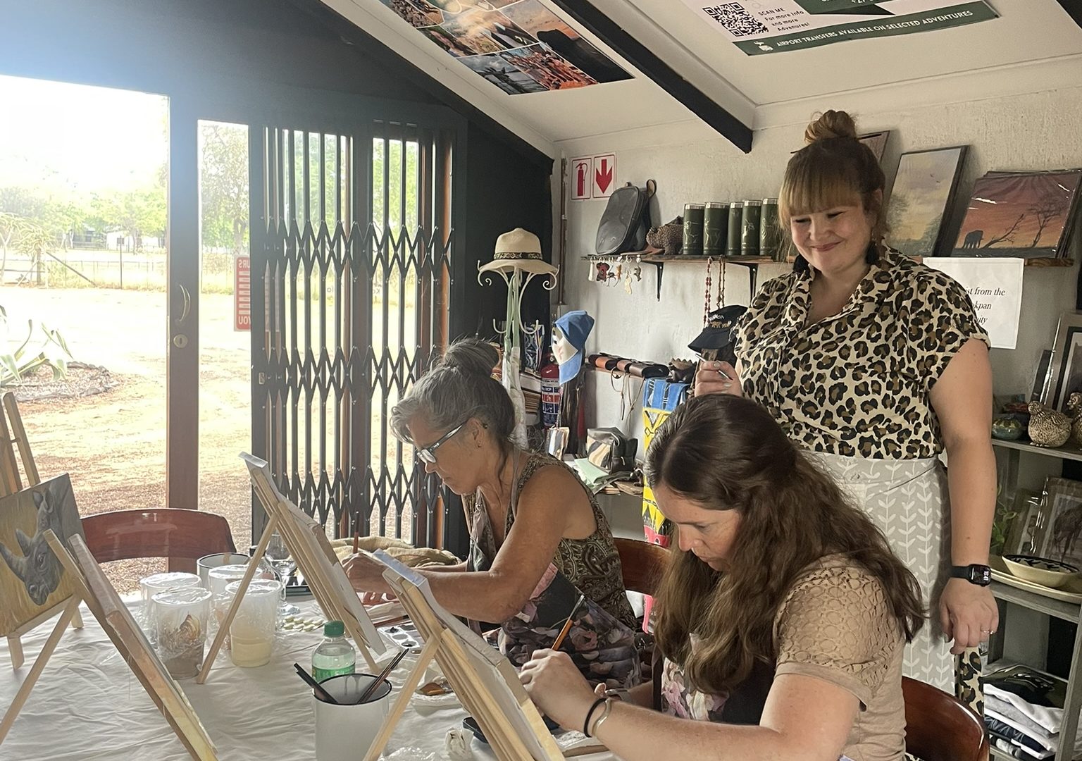 A tutor guiding a small group painting at tabletop easels.