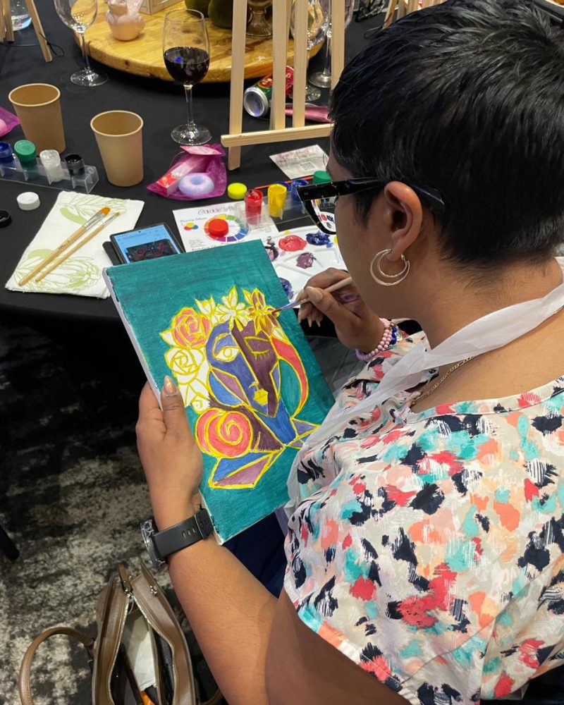 A participant painting a colourful abstract portrait at a paint-and-sip table.