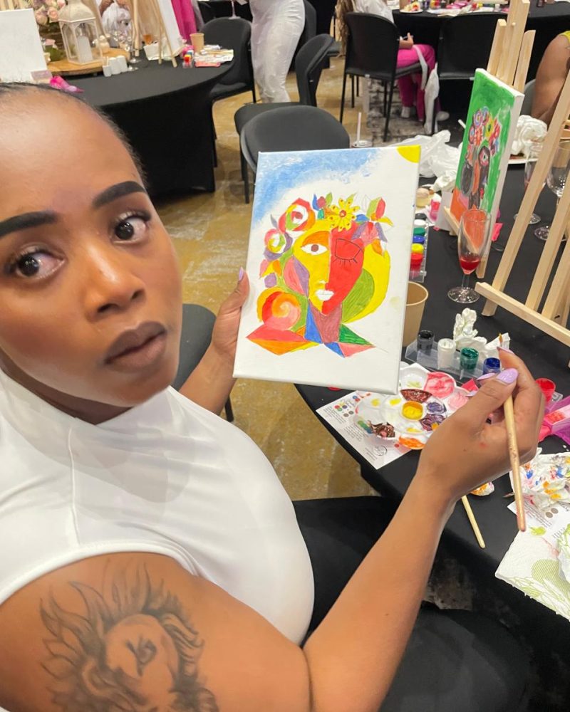 A participant holding up her colourful portrait painting at a paint-and-sip table.